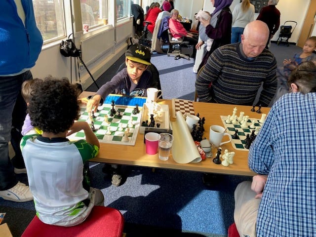 Children and adults playing chess together at a table in the ZNVA Warm Bank